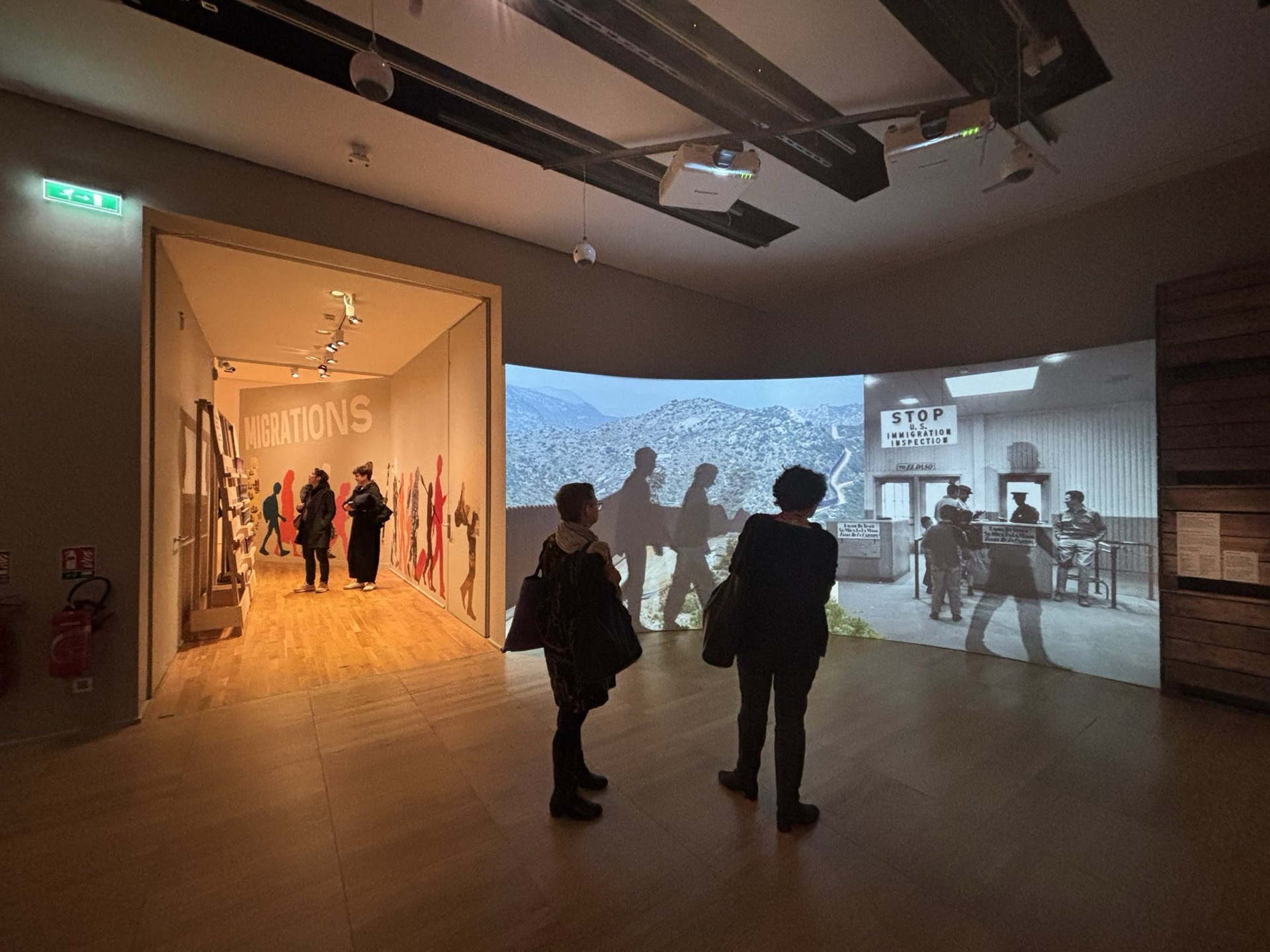 Visiteurs devant les portraits vidéo de l'exposition Migrations